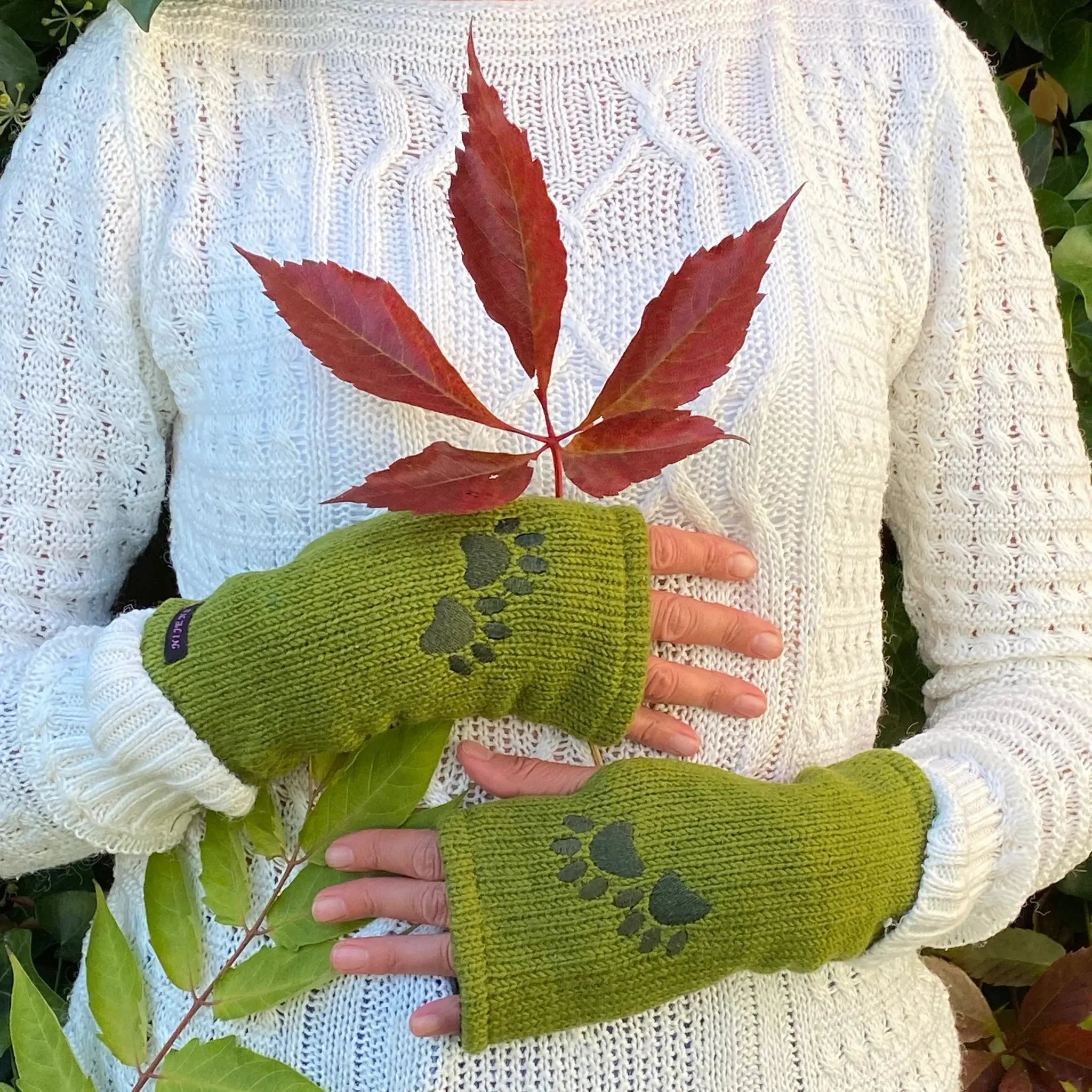 Handmodell mit Pulswärmer, Armstulpen mit Zwei-Pfoten-Stickerei aus Schurwolle in Grün. An der Seite gibt es einen Spalt für den Daumen.