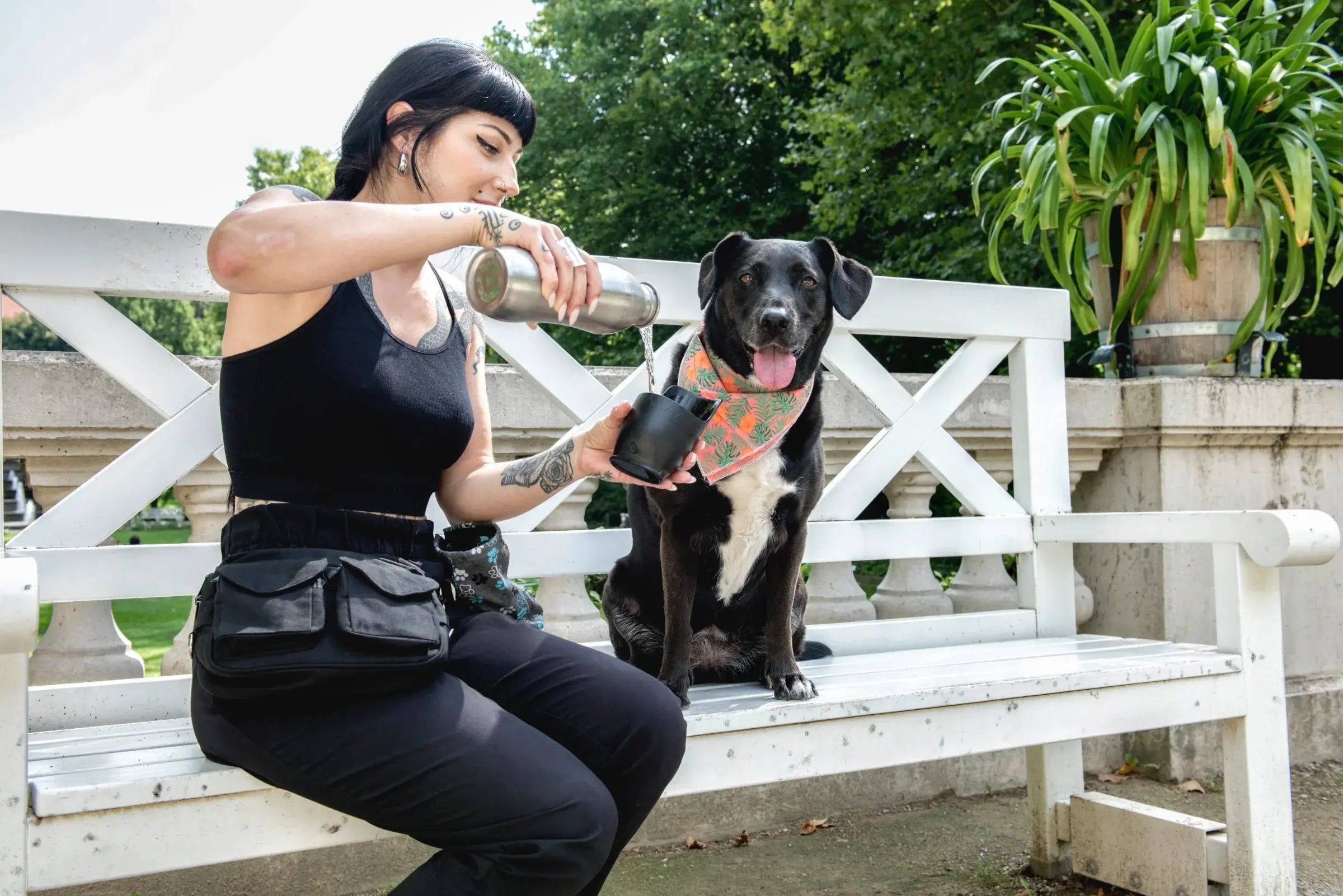 Eine Frau mit einer schwarzen Gassitasche von Nijens gießt Wasser für einen Hund