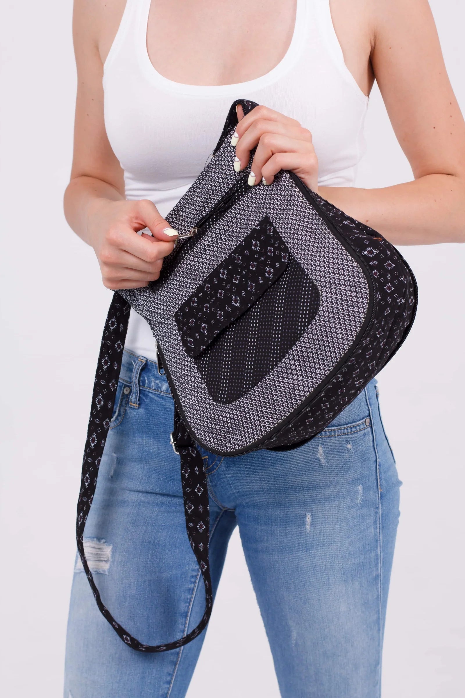 Frau in weißem Top und Jeans zeigt eine schwarze Nijens Umhängetasche mit dezentem geometrischem Muster und Fronttasche, während sie den Reißverschluss öffnet.
