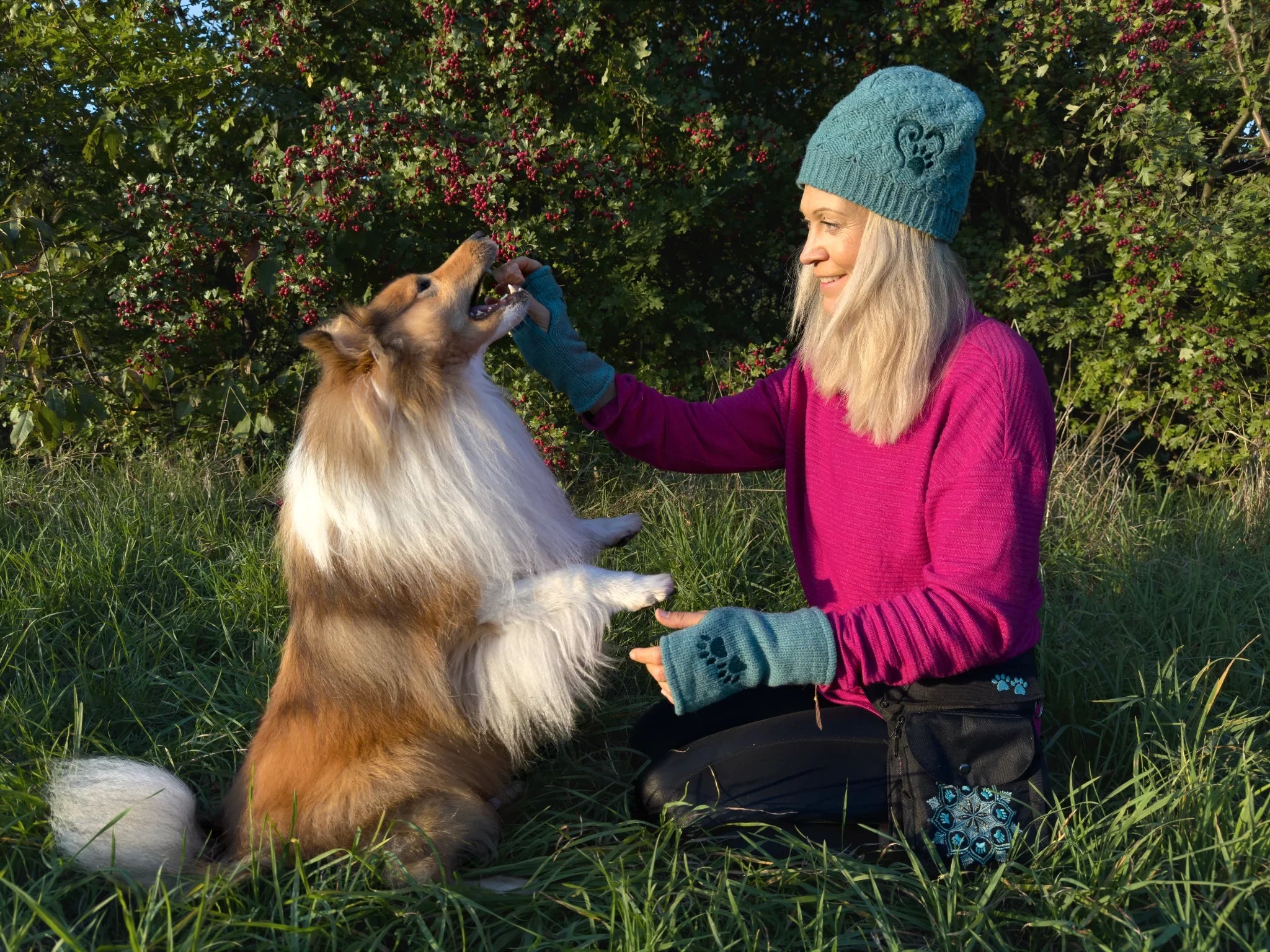 Frau beim Hundetraining im Herbst mit Collie, trägt petrolfarbene Wollmütze und passende Pulswärmer von Nijens – handgemachte Accessoires aus Schurwolle