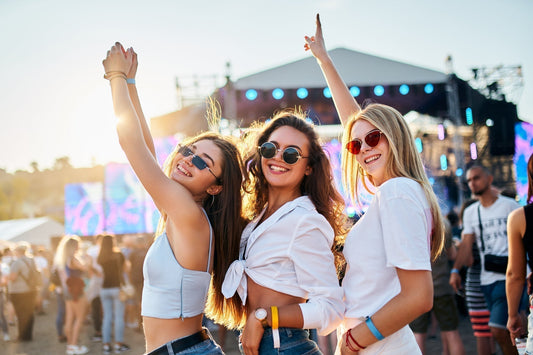 Symbolbild für Festival Packliste: 3 junge Frauen stehen auf einem Festivalgelände und lächeln