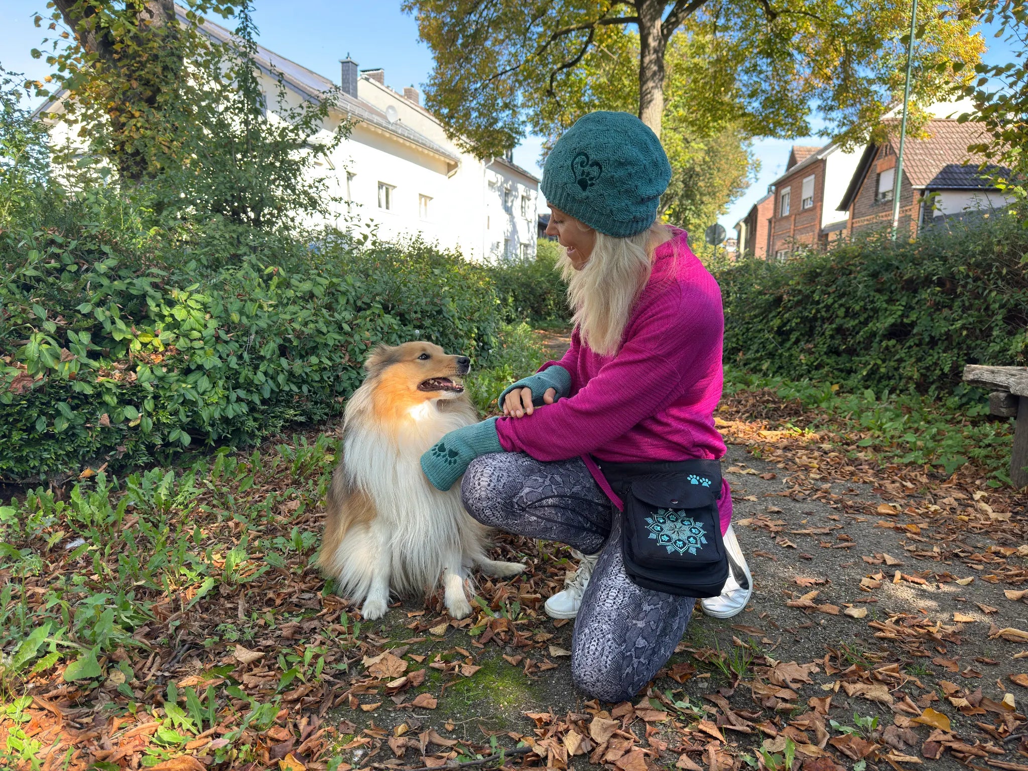 Frau trägt Nijens Beanie und Gassi-Tasche mit Mandala-Motiv beim Spaziergang mit ihrem Hund im herbstlichen Park