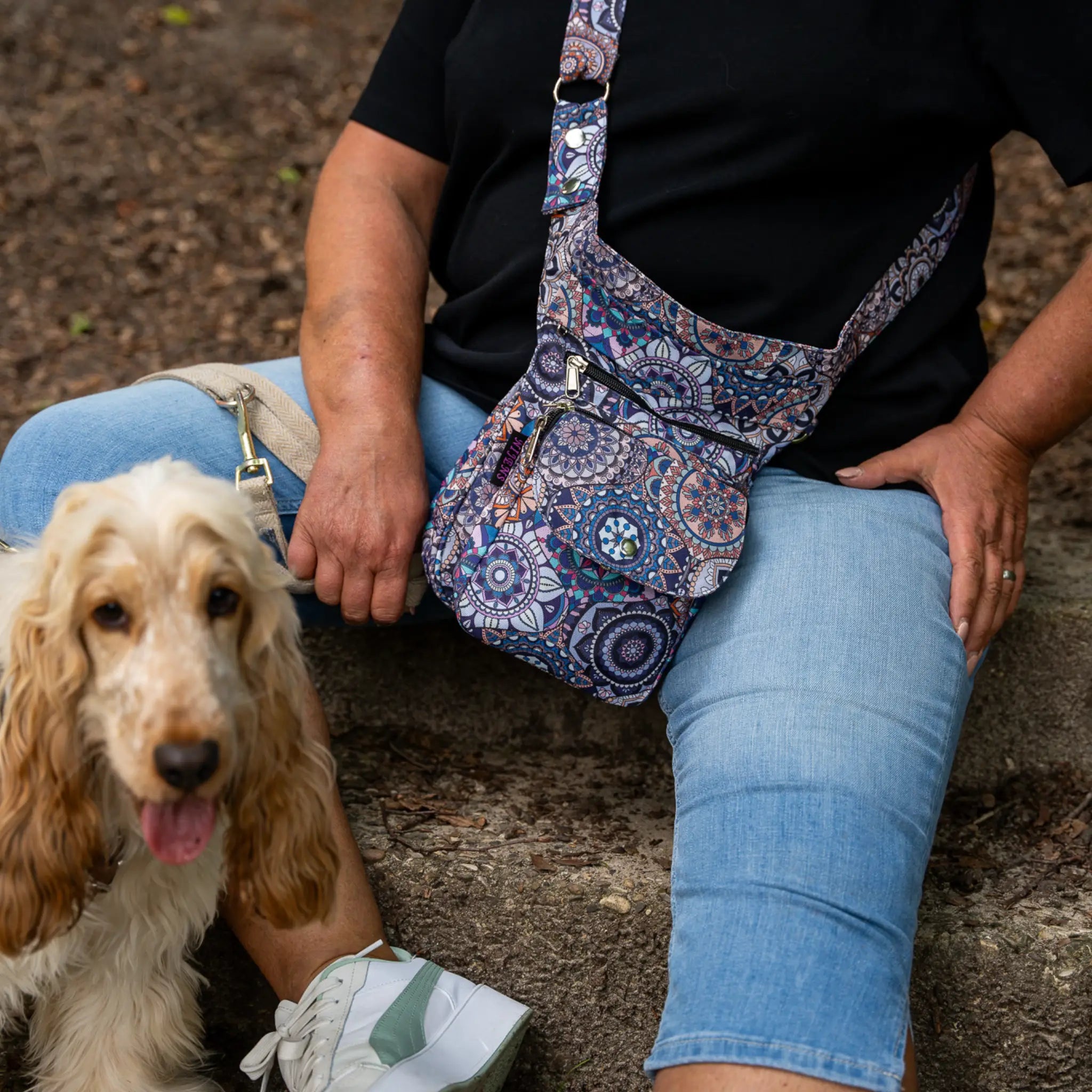 Frau mit Hund sitzt im Freien und trägt bunte Nijens Gassi-Tasche Super Hannover mit Mandala-Muster als Umhängetasche