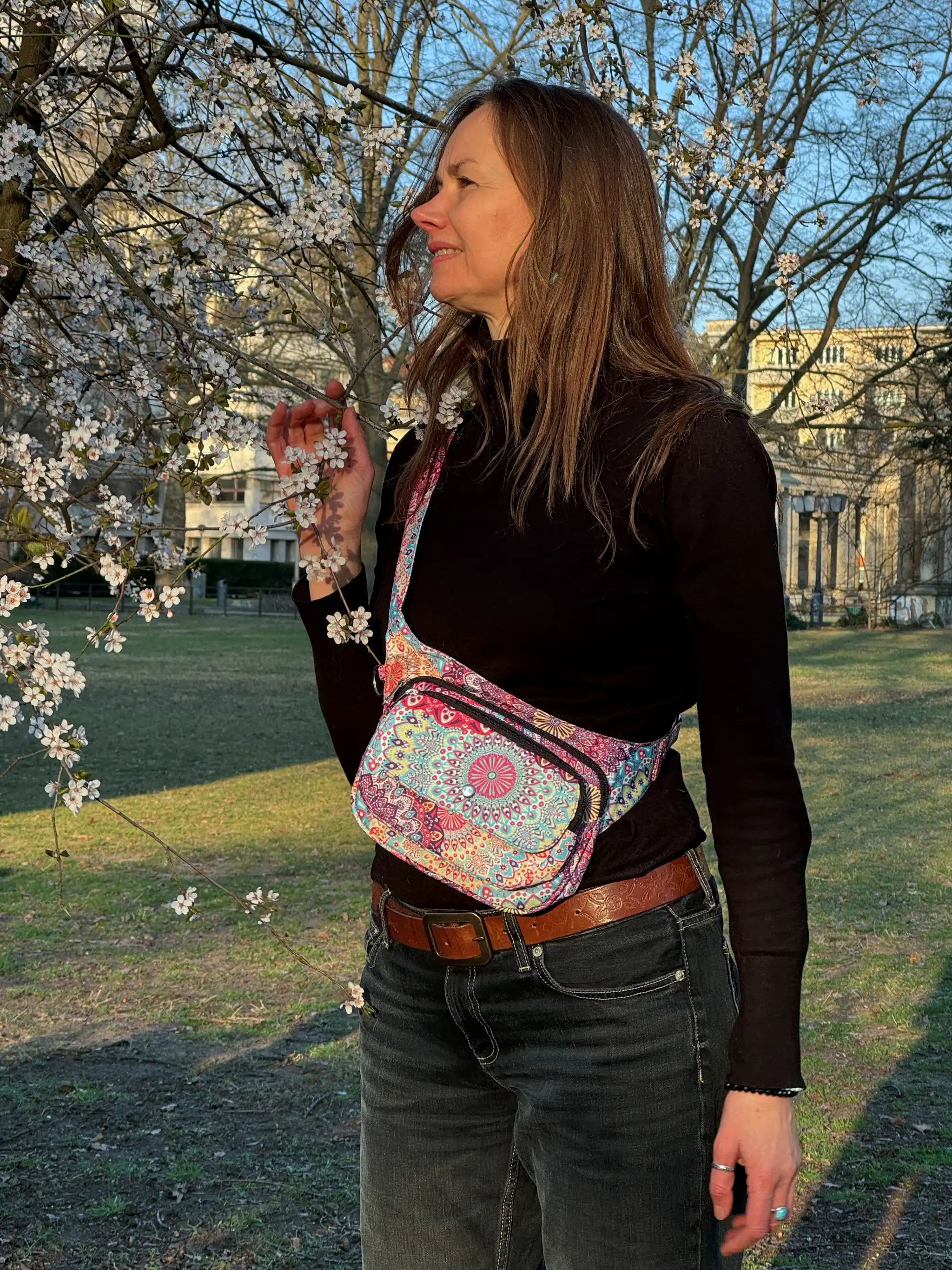 Bunte Festival-Bauchtasche mit Mandala-Muster von Nijens liegt am Ufer inmitten von Schilf und Natur, stimmungsvoll fotografiert bei Sonnenlicht.