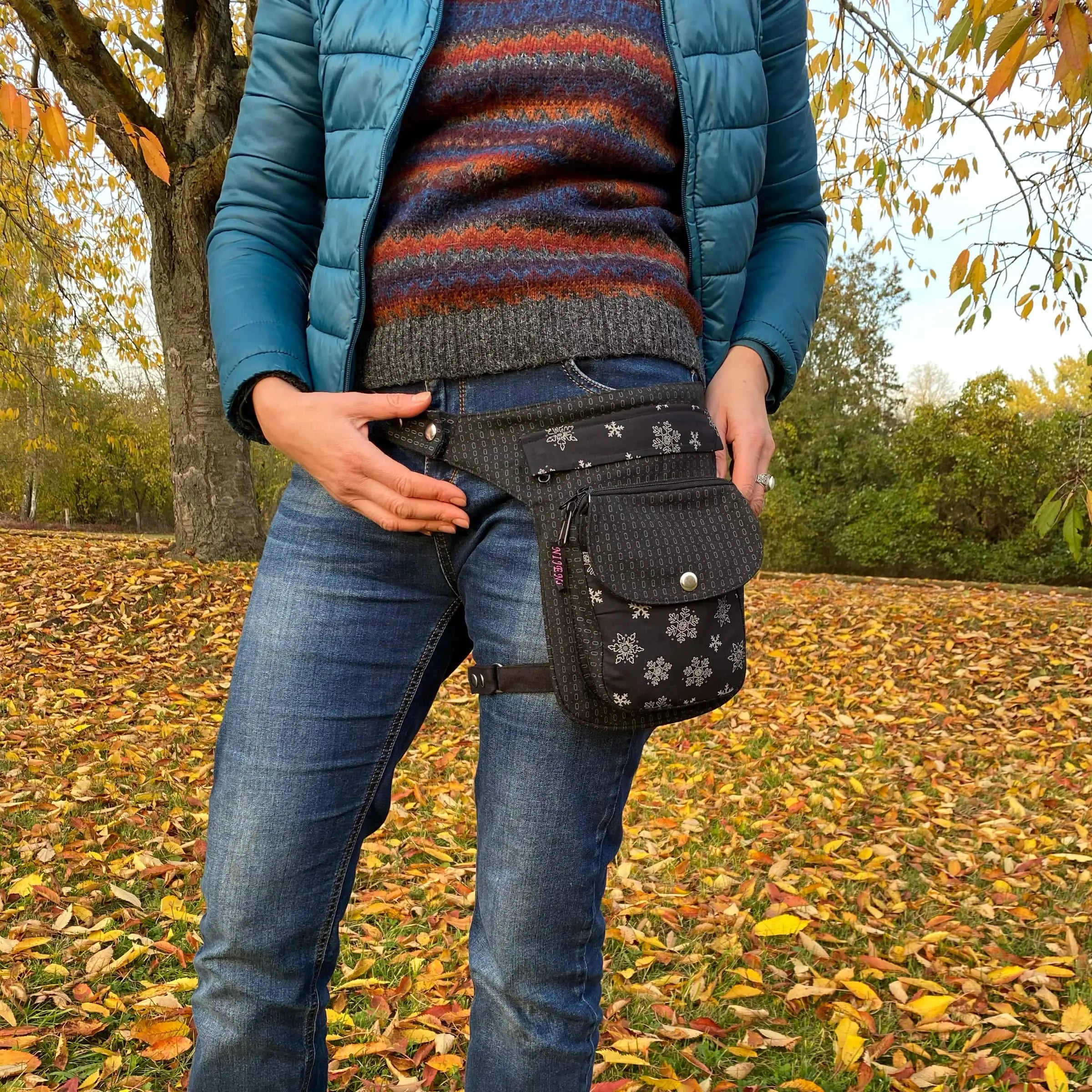 Bildausschnitt einer Frau in einer herbstlichen Parklandschaft. Die Frau präsentiert eine der Hüft-Gassitaschen Hannover, welche mit einem Beingurt am Oberschenkel fixiert werden kann.