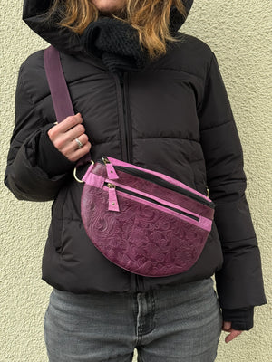 Nahaufnahme: Model präsentiert Crossbody-Bag aus Leder in Violett mit floraler Prägung. 