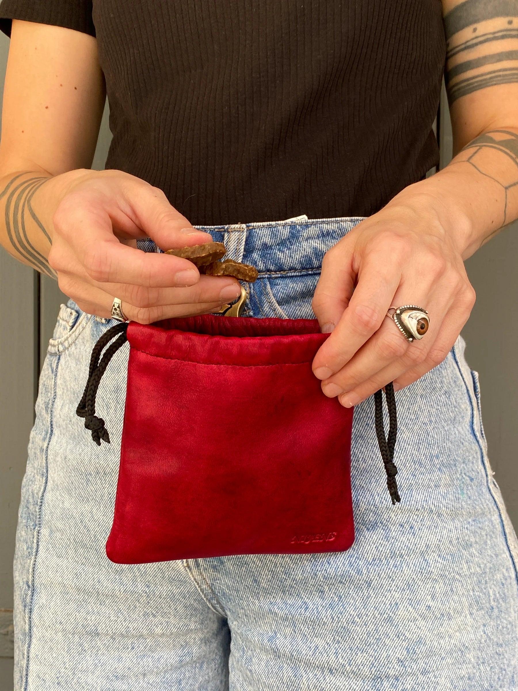 Eine Frau trägt eine rote Leder Leckerli-Tasche mit Karabiner und mit Zugkordel.