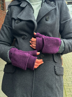 Nahaufnahme Hände: Model präsentiert Fäustlinge, Handstulpen mit Fingerkappe aus Schurwolle Lila. Die Fingerkappe wird mit einem Knopf auf der Handrückenseite fixiert.