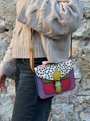Eine Frau trägt die kleine bunte Leder Umhängetasche mit Gepard-Muster, farbigem Leder in Lila, Rot, und Olivgrün sowie verstellbarem Schulterriemen. 