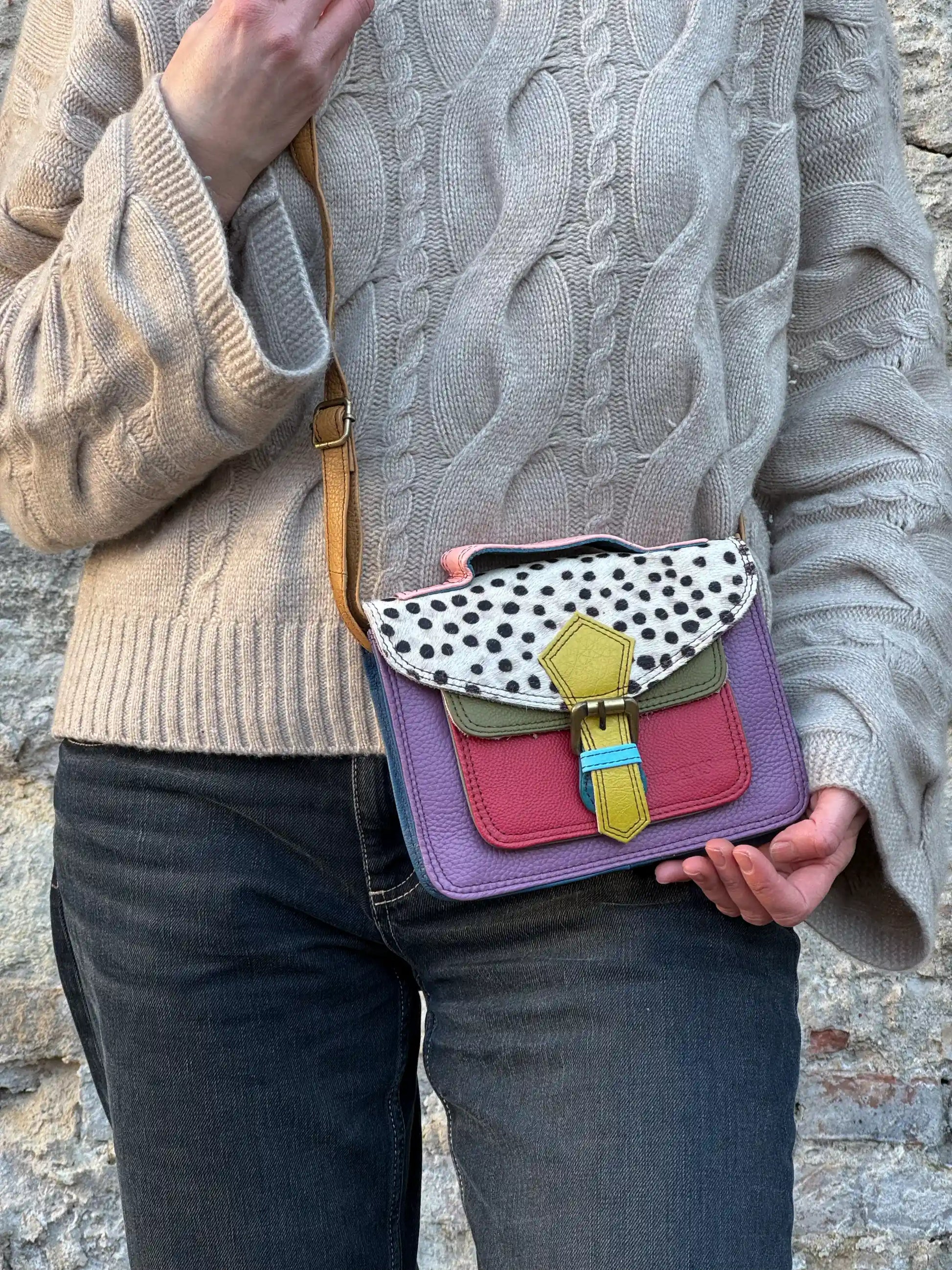 Eine Frau trägt  bunte Leder Umhängetasche mit Gepard-Muster, farbigem Leder in Lila, Rot, und Olivgrün sowie verstellbarem Schulterriemen. 