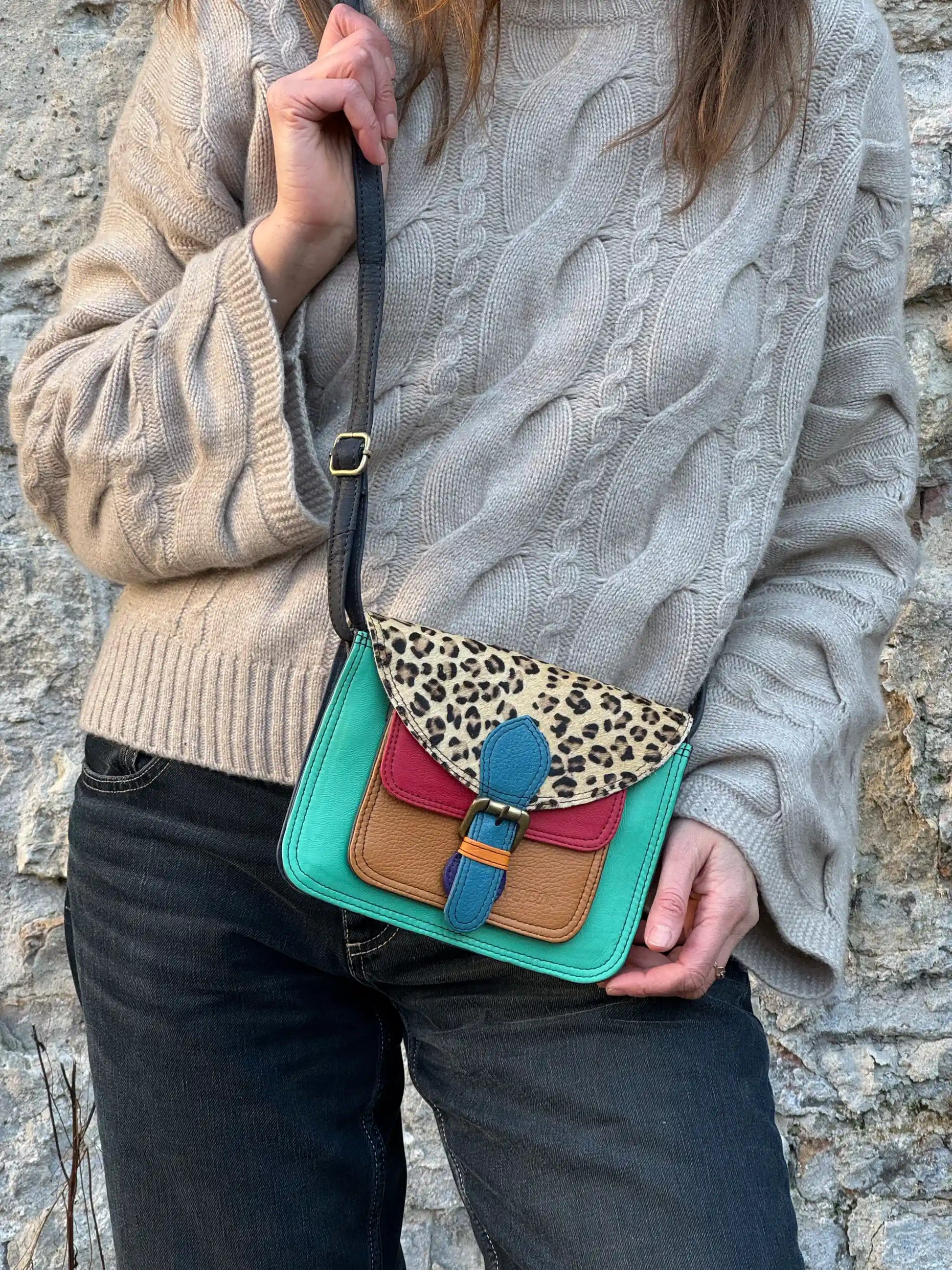 Eine Frau trägt bunte Leder Umhängetasche mit Leo-Muster, farbigem Leder in Türkis, Rot, Cognac und Blau sowie verstellbarem Schulterriemen.