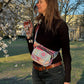 Frau trägt die bunte Mandala-Hüfttasche von Nijens als Crossbody-Bag über der Schulter, im Park mit blühenden Bäumen.
