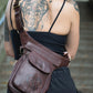             Weibliches Modell, Hinteransicht, präsentiert Gassitasche aus Leder Schockobraun mit Pfote-Herz-Prägung als Crossbodybag.
