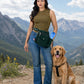 Frau mit tannengrüner Gassi-Tasche und goldenem Retriever auf einem Bergweg vor alpiner Kulisse mit Bergen.