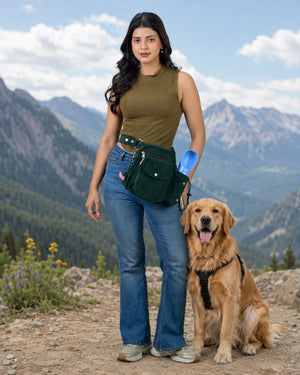 Frau mit tannengrüner Gassi-Tasche und goldenem Retriever auf einem Bergweg vor alpiner Kulisse mit Bergen.