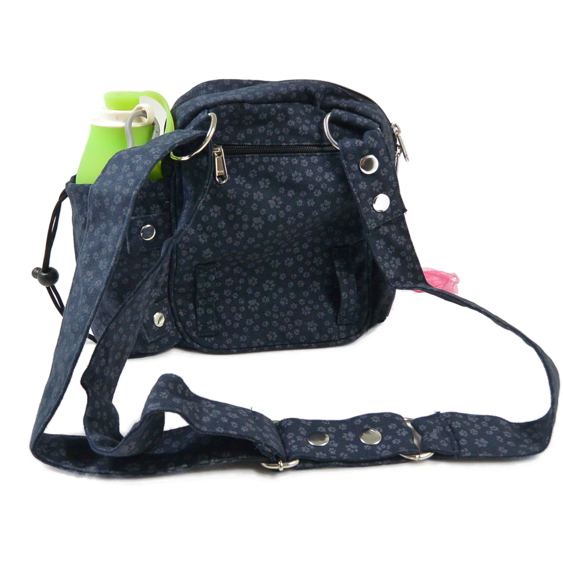 Rückansicht der dunkelblauen Gassitasche Konstanz mit Pfotenmuster von Nijens. Die Tasche ist mit verstellbarem Gurt, Reißverschlussfach auf der Rückseite, rosa Kotbeutelrolle und grün-weißer Hunde-Trinkflasche im seitlichen Flaschenfach ausgestattet.