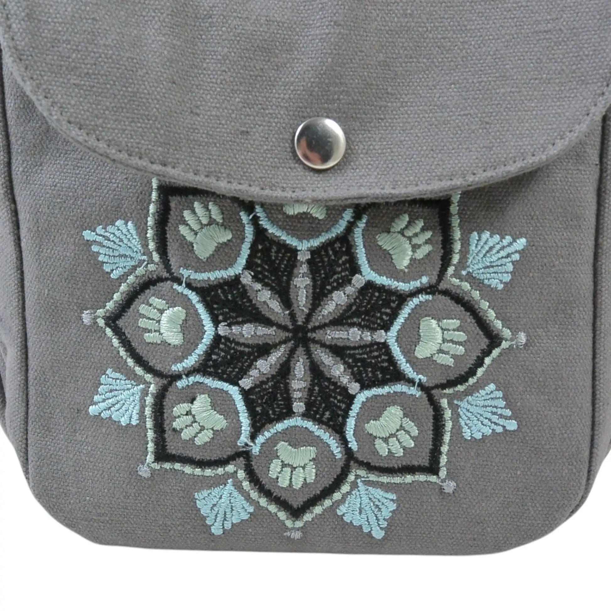 Detailaufnahme einer grauen Nijens Gassitasche mit Mandala-Stickerei in Grau-Türkis und Pfotenmotiv auf der Fronttasche.