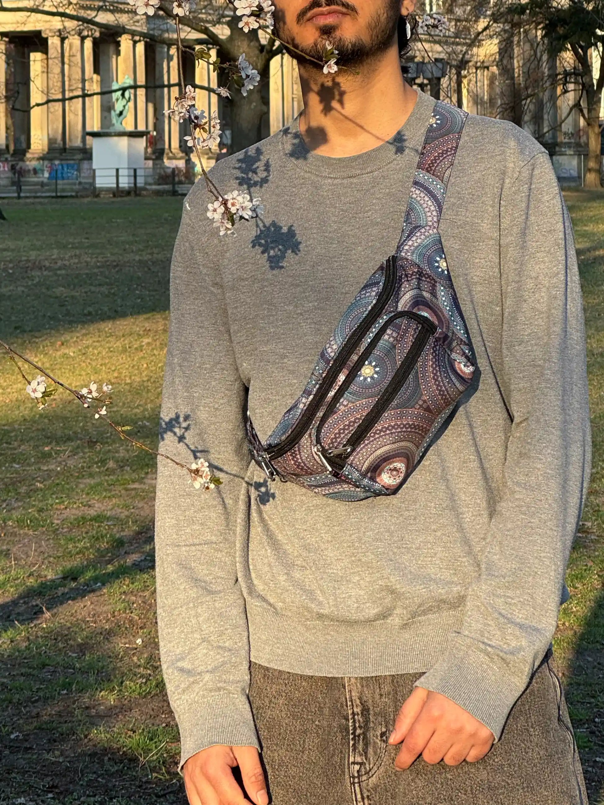 Crossbody Bag Torino mit Mandala-Muster in Blau getragen von Mann im Park mit blühenden Bäumen
