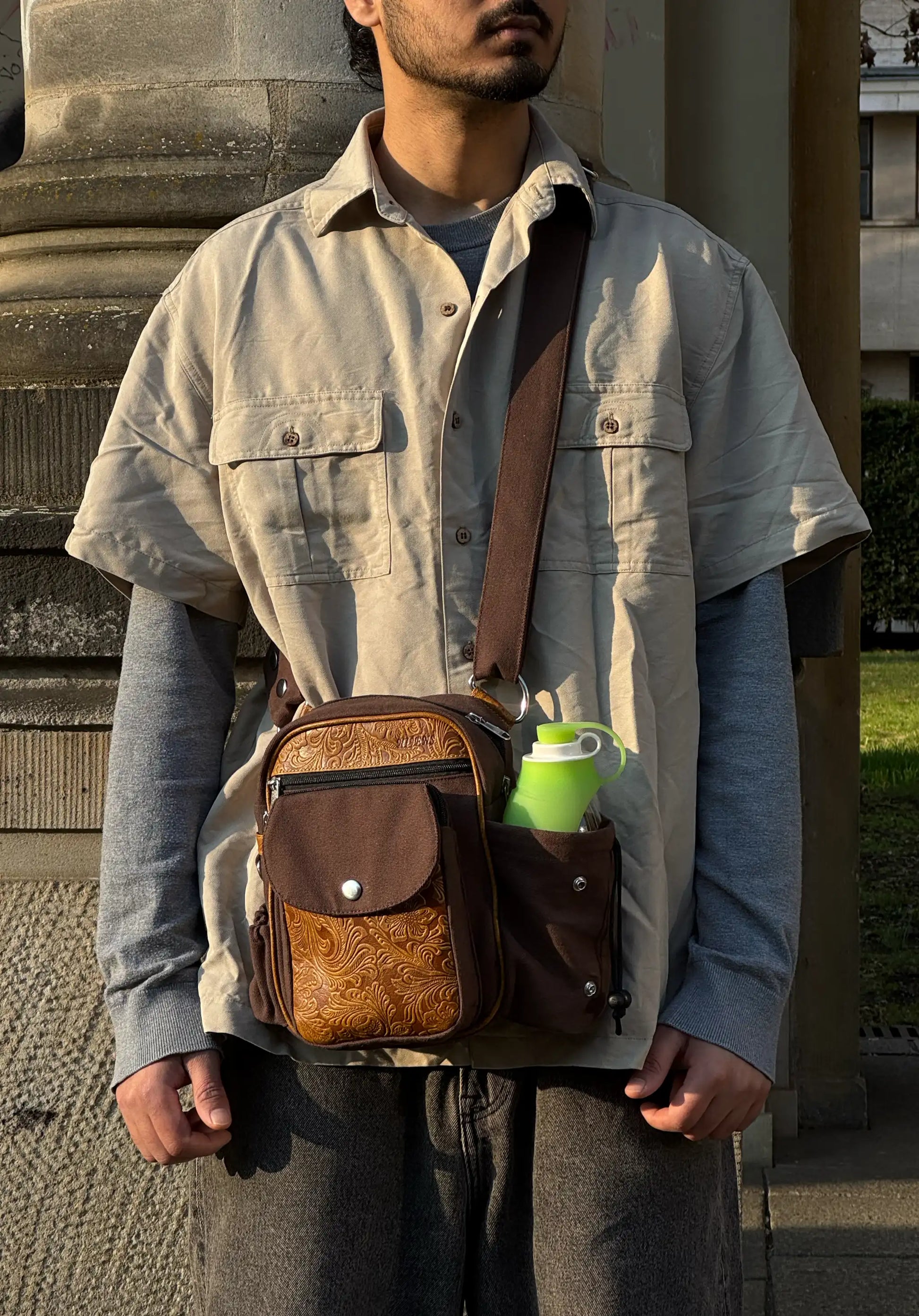 Mann trägt braune Leder Gassi-Tasche Konstanz im Vintage Stil mit Flaschenhalter und geprägtem Muster, als Crossbody Tasche im Alltag