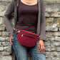 Frau trägt eine weinrote Crossbody Bag aus Cord mit Reißverschlussfächern lässig vor einer Natursteinmauer.