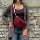 Frau trägt weinrote Cord Crossbody Bag lässig über der Schulter vor einer Natursteinmauer