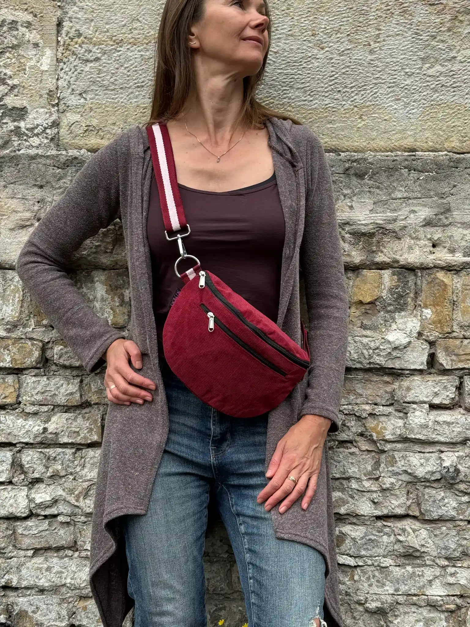 Frau trägt weinrote Cord Crossbody Bag lässig über der Schulter vor einer Natursteinmauer