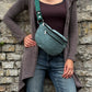 Frau trägt salbeigrüne Cord Crossbody Bag lässig über der Schulter vor einer Natursteinmauer