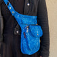 Model präsentiert Gassi-Tasche, Bauchtasche und Gürteltasche aus Polyesterblau mit floralen Elementen in der Tragevariante Crossbodybag.