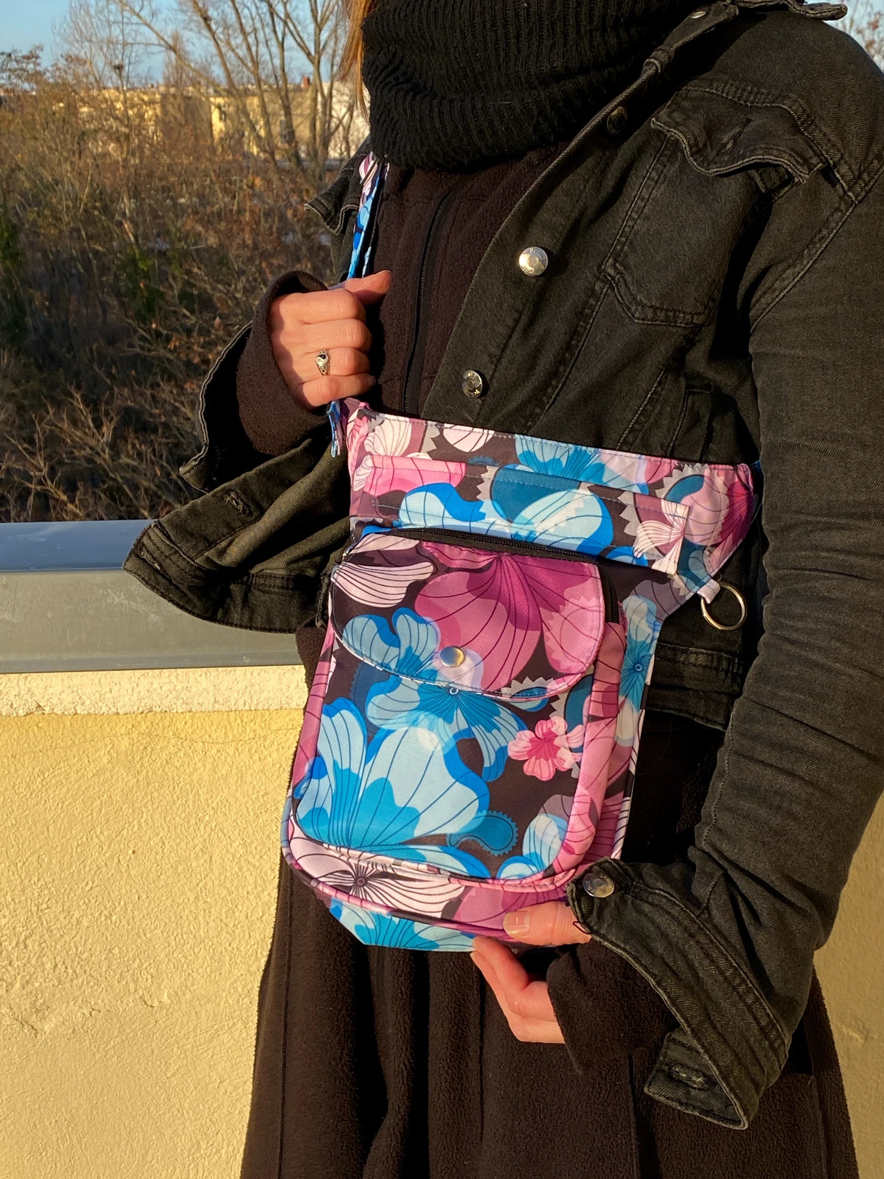 Model präsentiert Gassi-Tasche, Bauchtasche und Gürteltasche aus Polyester Blau , Magentafarben mit Blumenblätter Motiven in der Tragevariante Crossbodybag.