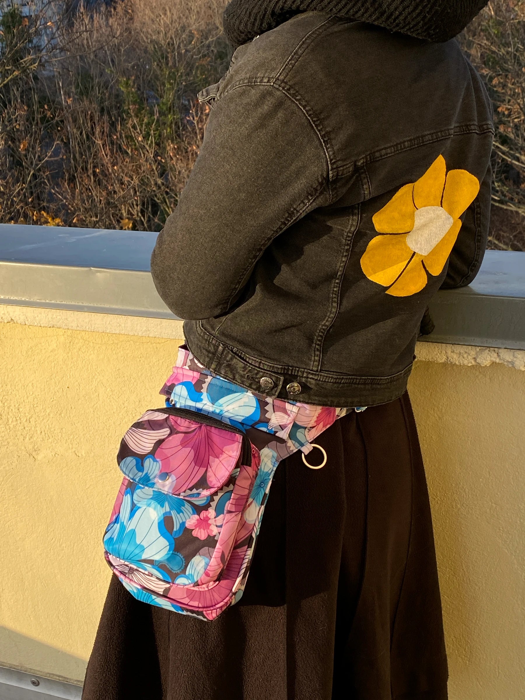 Model präsentiert Gassi-Tasche, Bauchtasche und Gürteltasche aus Polyester Blau , Magentafarben mit Blumenblätter Motiven in der Tragevariante Bauchtasche.