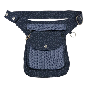 Gassi-Tasche aus Canvas- Stoff Violett mit kleinen Pfotenmotiven mit zwei Reißverschlussfächer vorne sowie einem Einsteckfach, welches durch einen Überschlag mit einem Druckknopf verschlossen wird. Auf der hinteren Seite befindet sich ein weiteres Reißverschlussfach. An der Seite des Taschengurtes befindet sich ein kleiner Metallring und zum Anhängen kleiner Beuteltaschen.