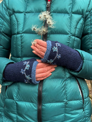 Model präsentiert Handstulpen mit Daumen aus Schurwolle Dunkelblau und Hellblau, bestickt mit Blumengirlande. Jede Blume besitzt mittig ein Strasssteinchen.