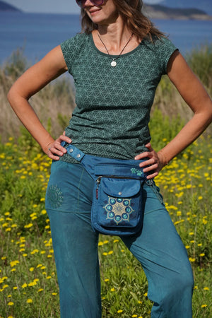 Frau in der Natur mit blauer Nijens Gassitasche Hannover mit Mandala-Stickerei, getragen als Hüfttasche beim Spaziergang im Grünen.