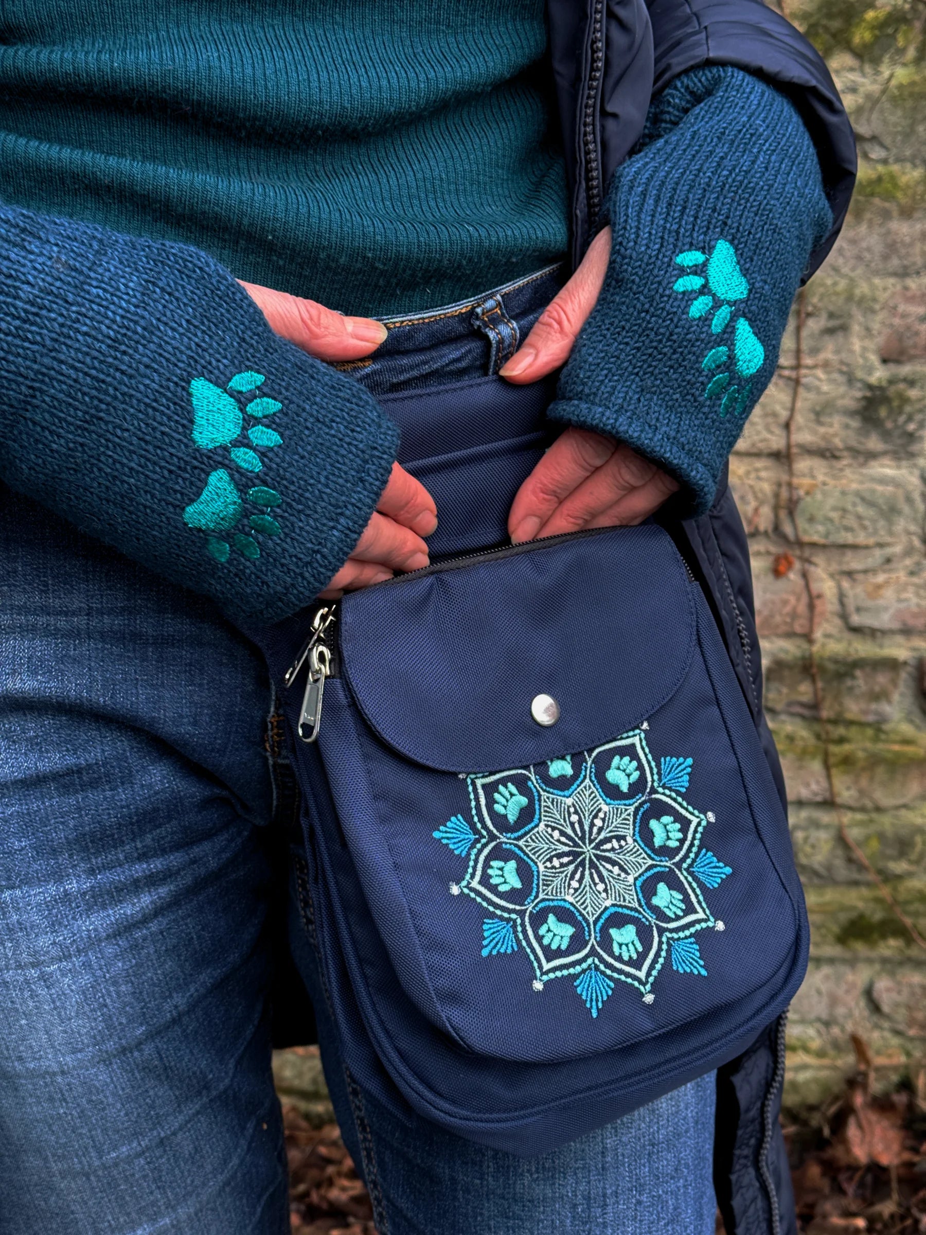 Model präsentiert Gassi-Tasche, Gürteltasche Hannover Mandala 313 aus wasserabweisendem Nylonstoff in Dunkelblau mit Pfoten-Mandala-Sttickerei. An den Händen trägt sie Handstulpen HADAR 16 aus Schurwolle Dunkelblau mit zwei Pfotenstickerei.