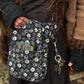 Nahaufnahme Bauchtasche: Model präsentiert Gassi-Tasche, Bauchtasche Hannover aus Baumwoll-Canvas in Schwarz mit großen Pfoten-Prints. Vorne befindet sich ein verschließbares Einsteckfach. Am Gurt gibt es einen Schlüsselring, an dem ein Schlüssel mit Karabiner hängt. Sie trägt an den Händen Handstulpen mit Daumen aus Schurwolle, schwarz.
