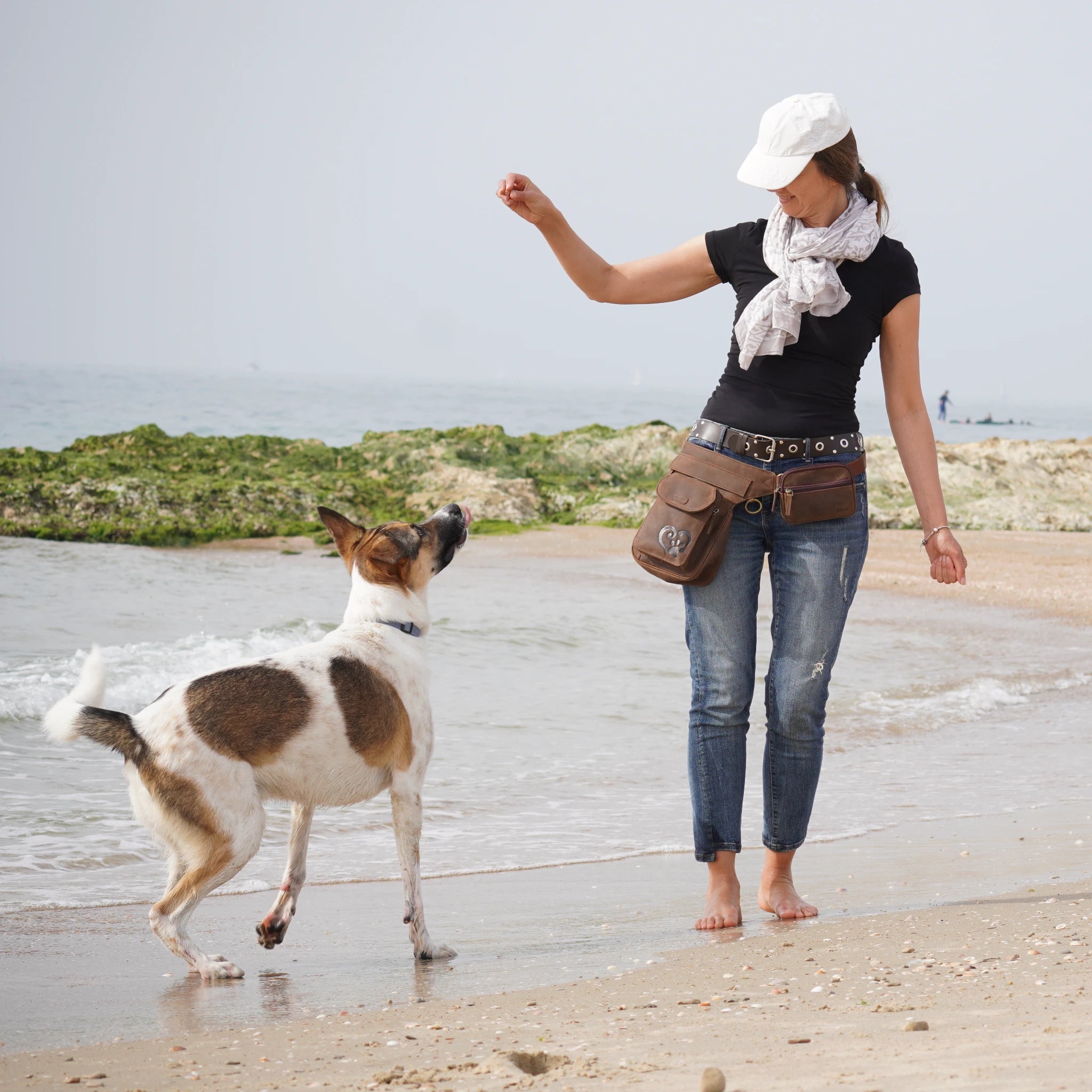 Frau mit brauner Nijens Leder-Gassi-Tasche spielt mit ihrem Hund am Strand.