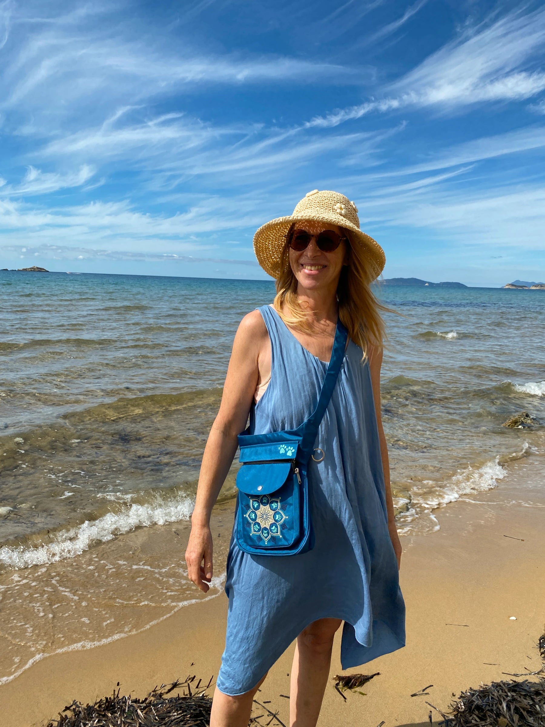 Gassitasche für Hundebesitzer, Bauchtasche aus wasserabweisendem Nylonstoff Petrol-Türkis mit Blumenpfotenmandala-Stickerei. Am Ufer gegen das blaue Meer. Corfu.