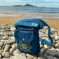 Gassitasche, Bauchtasche aus wasserabweisendem Nylonstoff Petrol-Türkis mit Blumenpfotenmandala-Stickerei. Am Ufer gegen das blaue Meer.