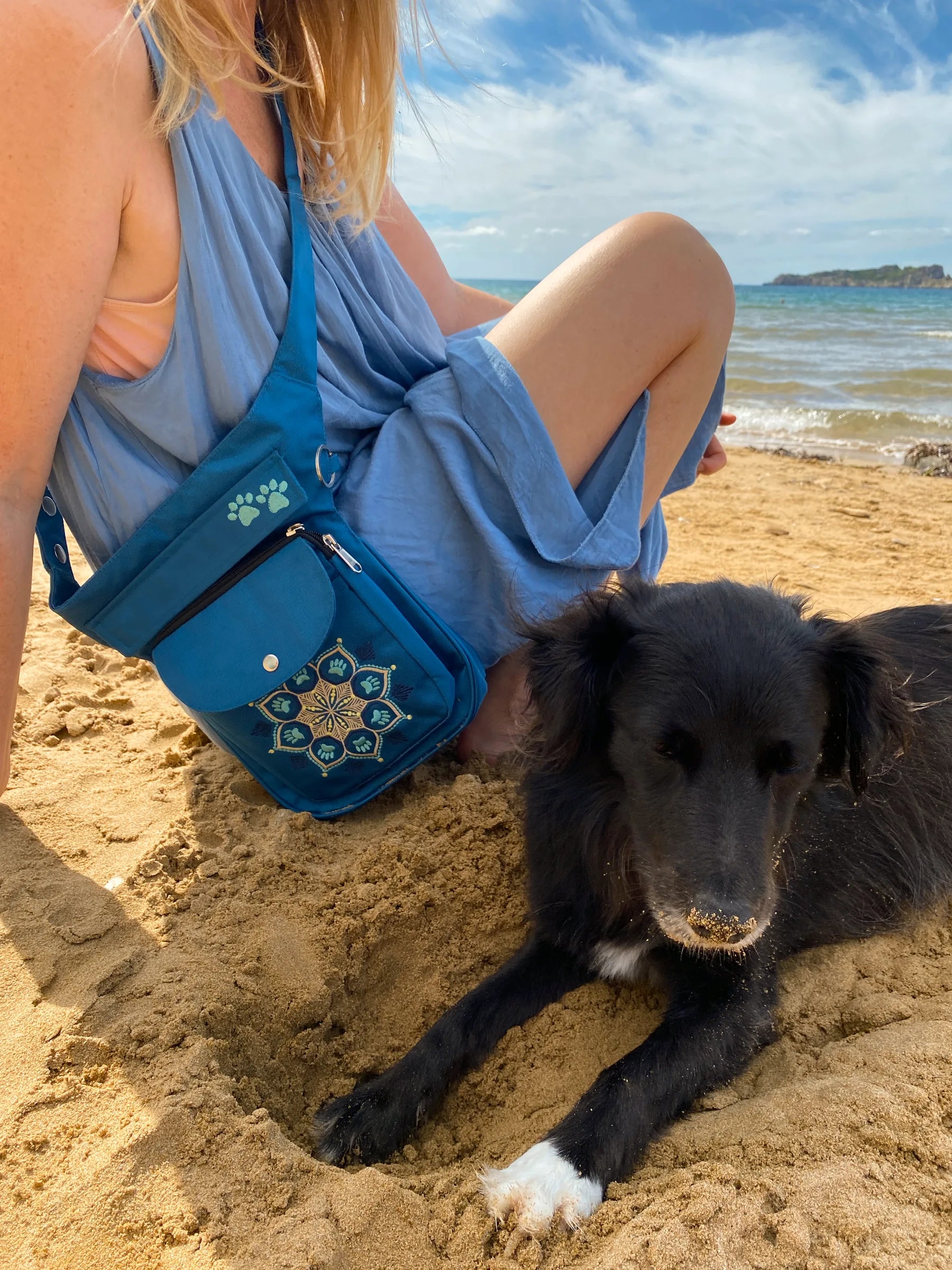 Gassitasche für Hundebesitzer, Bauchtasche aus wasserabweisendem Nylonstoff Petrol-Türkis mit Blumenpfotenmandala-Stickerei. Am Ufer gegen das blaue Meer.