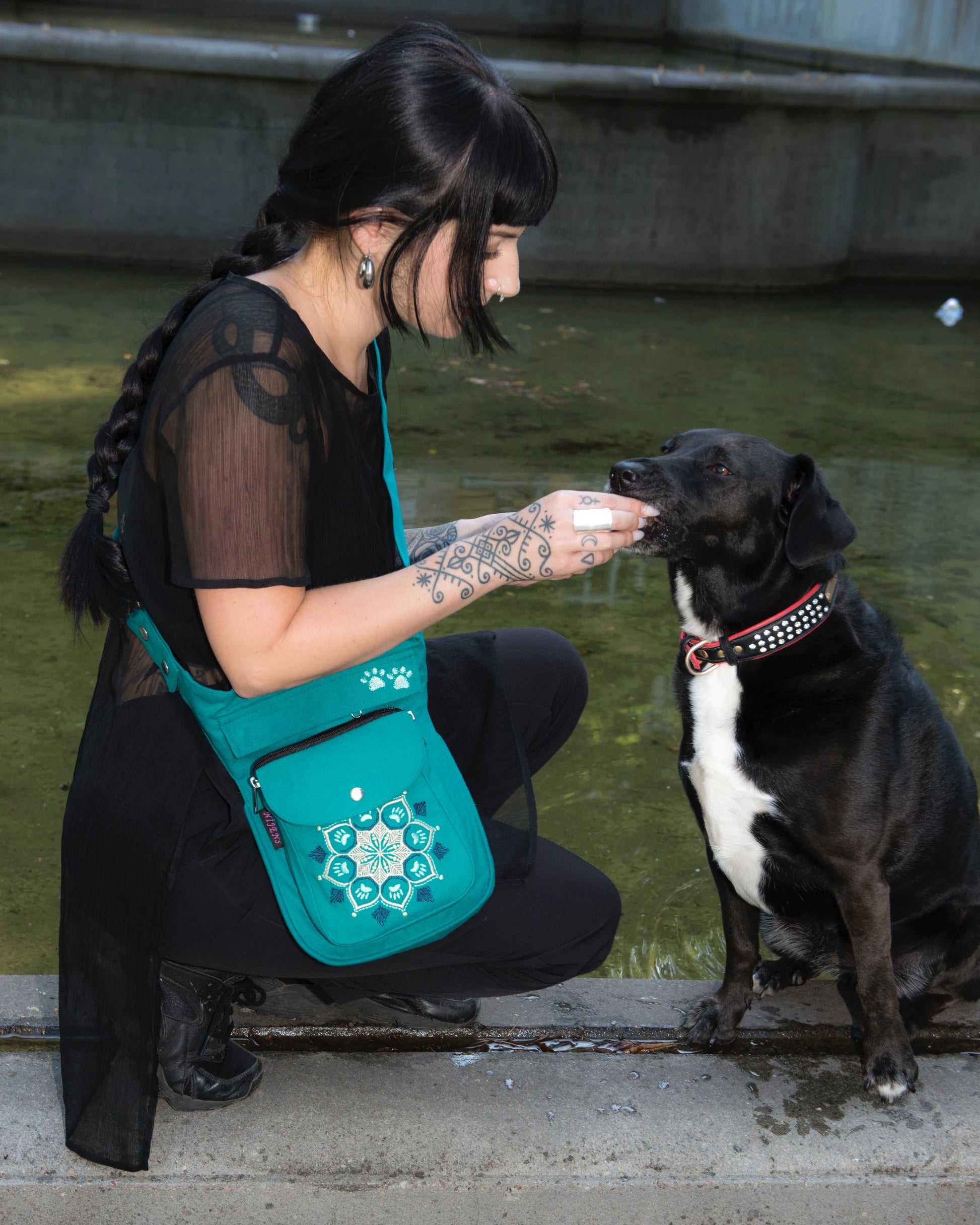 Die Frau nimmt Hundefutter aus einem türkisfarbenen Beutel mit einem schönen Mandala mit Pfotenstickerei und gibt es einem schwarzen Hund.