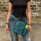 Frau mit schwarzem Oberteil und Jeans trägt eine petrolfarbene Nijens Gassi-Tasche mit Flaschenfach