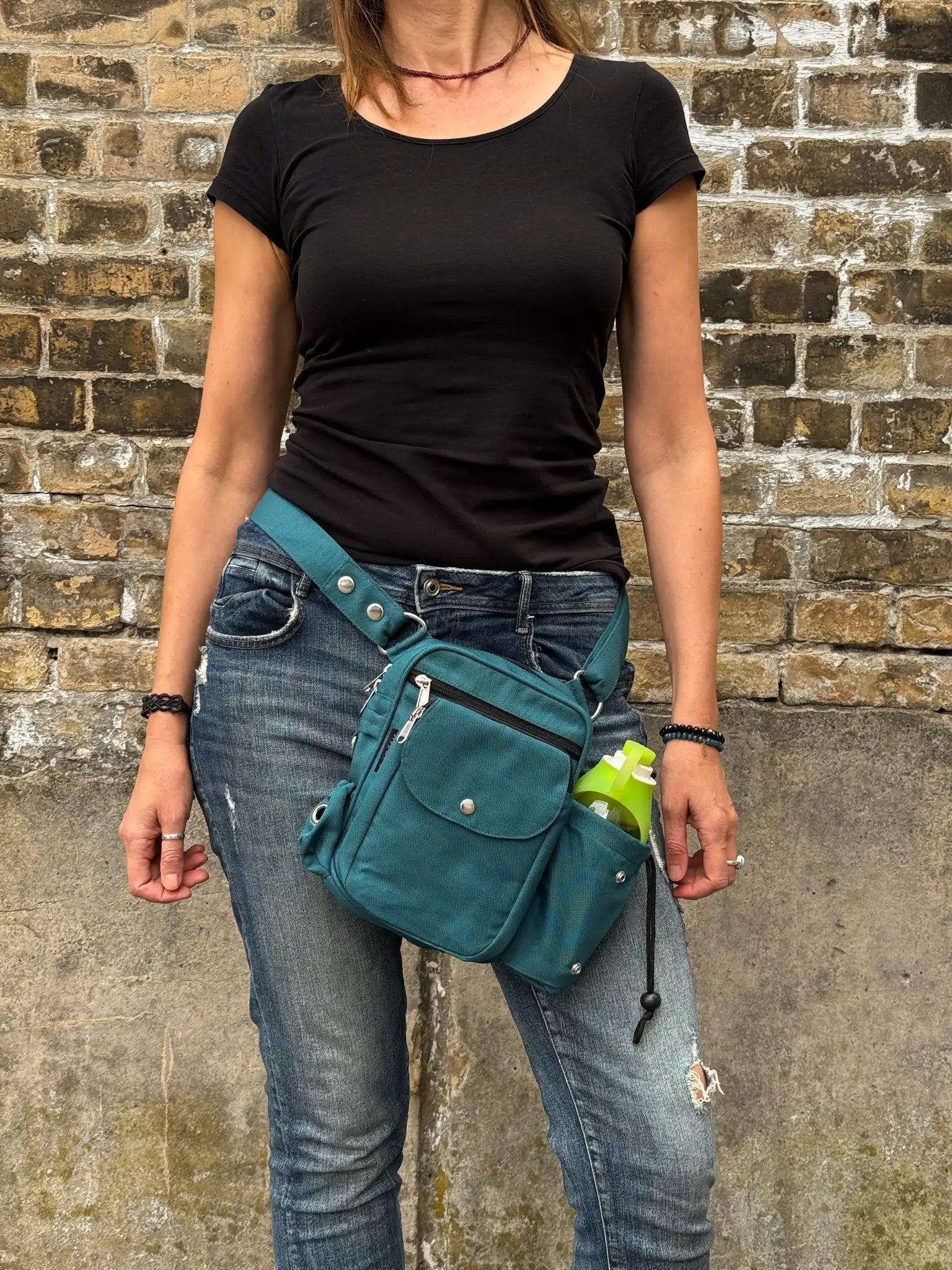 Frau mit schwarzem Oberteil und Jeans trägt eine petrolfarbene Nijens Gassi-Tasche mit Flaschenfach