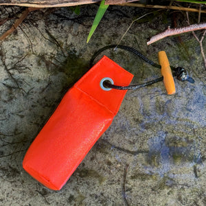 Kleiner oranger Wurf-Dummy für Hunde liegt am Ufer im flachen Wasser – ideal fürs Apportiertraining