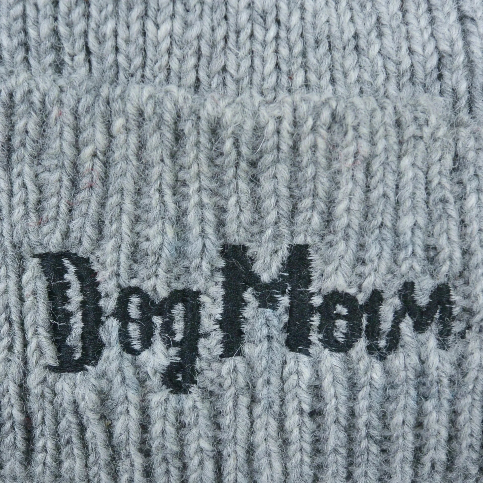 Nahaufnahme von dem gestickten „Dog Mom“-Schriftzug auf Wollmütze, Strickmütze und Beanie-Mütze aus Schurwolle, Hellgrau.