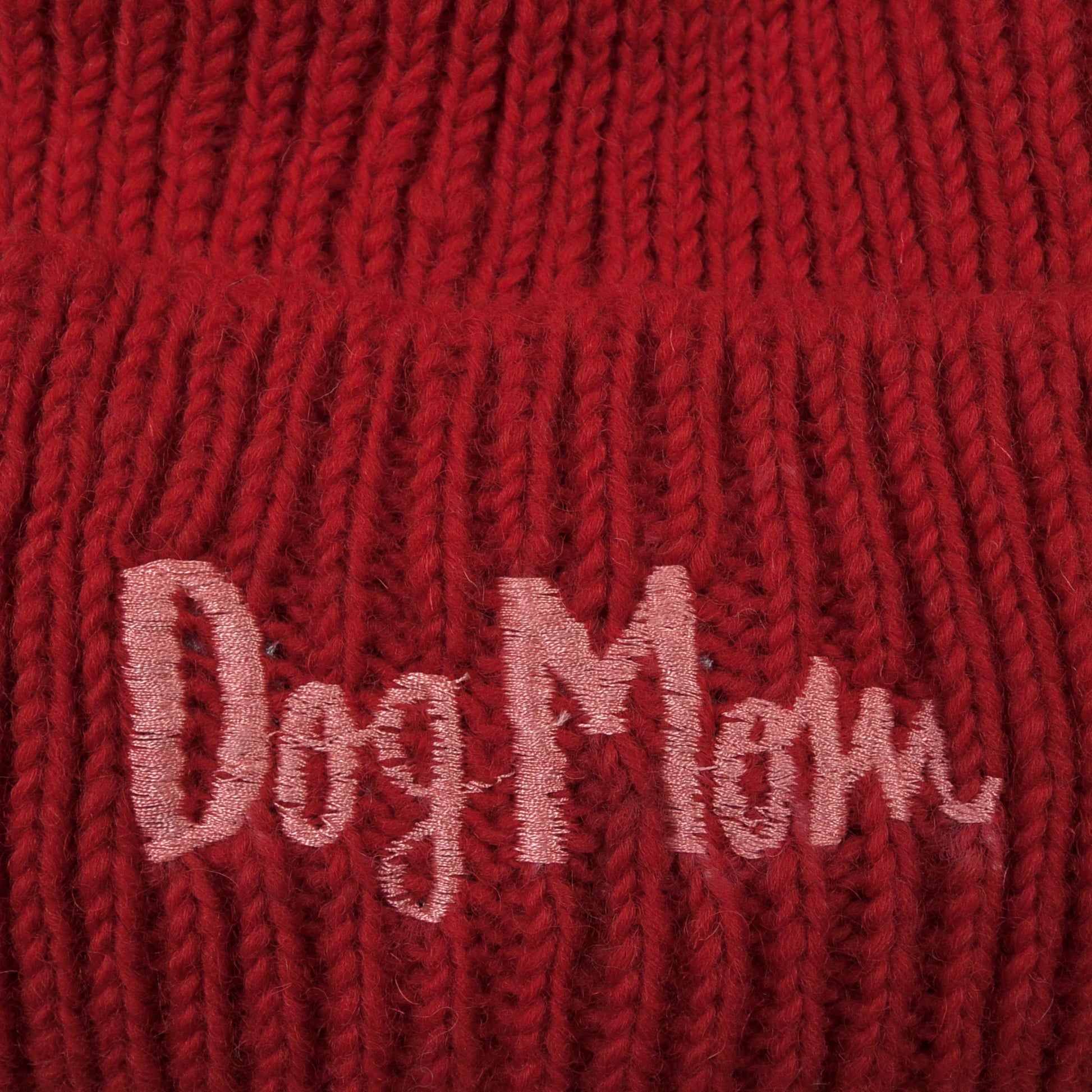 Nahaufnahme von dem gestickten „Dog Mom“-Schriftzug auf Wollmütze, Strickmütze und Beanie-Mütze aus Schurwolle, Feuerrot.