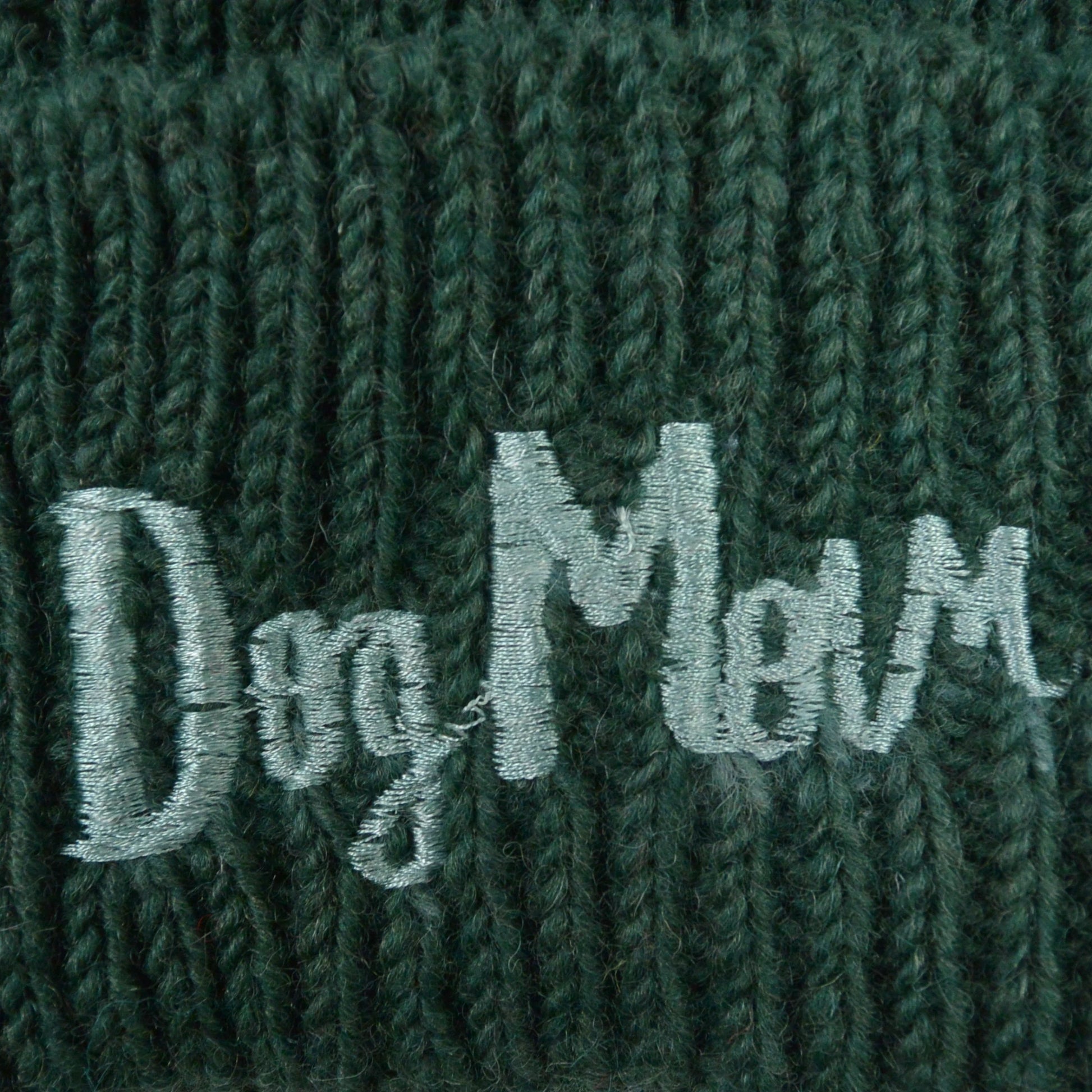 Nahaufnahme von dem gestickten „Dog Mom“-Schriftzug auf Wollmütze, Strickmütze und Beanie-Mütze aus Schurwolle, Dunkelgrün.