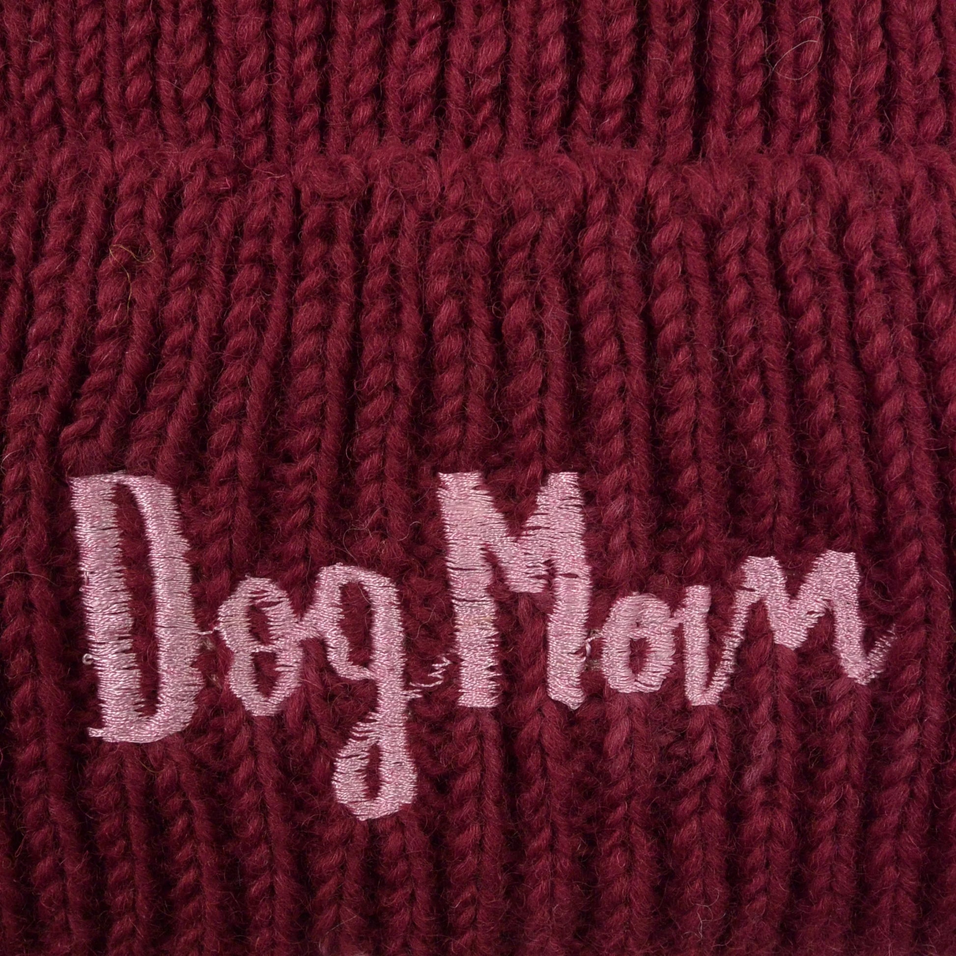 Nahaufnahme von dem gestickten „Dog Mom“-Schriftzug auf Wollmütze, Beanie-Mütze aus Schurwolle, Dunkelrot.