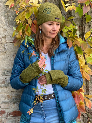 Model präsentiert  in herbstlicher Kulisse die kurze Beanie-Mütze, Strickmütze aus Schurwolle, Grün, bestickt mit Pfote-Herz-Logo und Handstulpen aus Schurwolle, Grün, mit Fingerkappe.