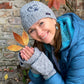 Model präsentiert die kurze Beanie-Mütze, Strickmütze aus Schurwolle, Grau, bestickt mit Pfote-Herz-Logo und Handstulpen aus Schurwolle Grau mit Fingerkappe.
