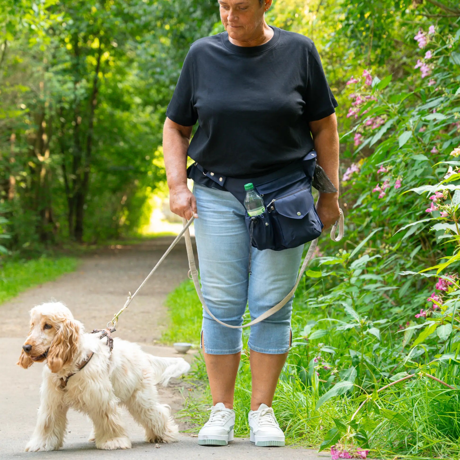Wasserabweisende dunkelblaue Gassi-Tasche Brandenburg mit Flaschenhalter beim Spaziergang mit Hund im Grünen getragen